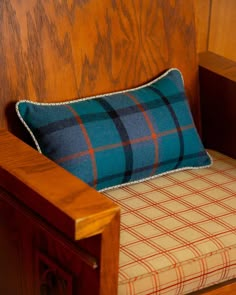 a wooden chair with a plaid pillow on it's armrest and seat cushion