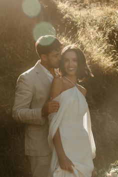 a man and woman standing next to each other in front of some grass with sunlight shining on them