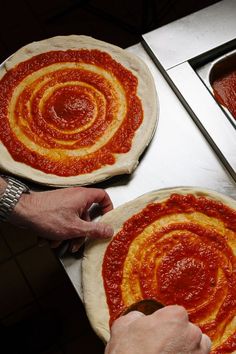 two uncooked pizzas with sauce on them are being prepared for the oven