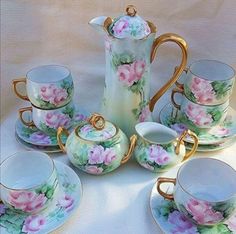 a tea set with pink flowers and gold trimmings sits on a white tablecloth