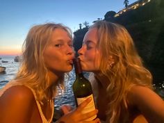 two beautiful young women kissing each other with a bottle of wine in front of them