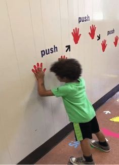 a young child is writing on the wall with his handprints and pointing to push button