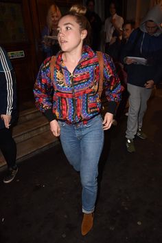 a woman walking down the street with her hand in her pocket and wearing a colorful jacket