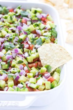 a white casserole dish filled with chopped vegetables and tortilla chips on the side