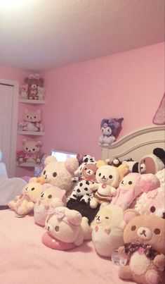 a bed with lots of stuffed animals on it in a room that has pink walls