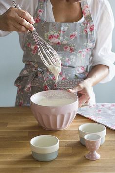 a woman in an apron whisks cream into a bowl with two small bowls next to her