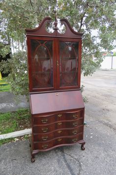 an old wooden dresser with glass doors on it's top and bottom drawers, sitting in front of a tree