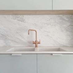 a white kitchen with marble counter tops and gold faucet in the sink area