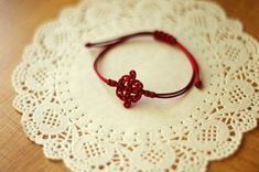 a red string bracelet sitting on top of a white doily with a knot in the middle