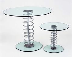 two glass tables with metal spirals on each side and one table has a round glass top