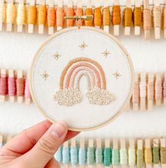 someone is holding up a small embroidery hoop with a rainbow in the middle and stars on it