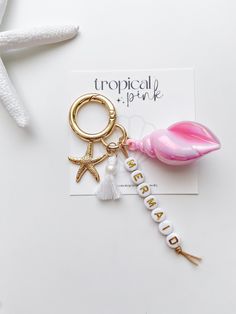 a keychain with a pink flower and starfish on it, sitting next to a card that says tropical pink