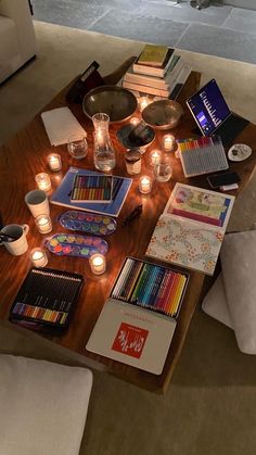 a coffee table filled with lots of art supplies on top of a wooden table covered in candles