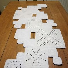 several crocheted squares are laid out on a wooden table with a chair in the background