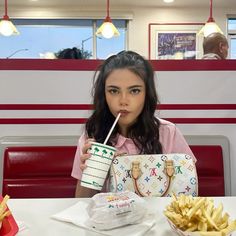 a woman sitting at a table with a drink and some french fries