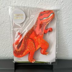 an orange and red toy lizard on display in a plastic package with white wall behind it