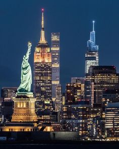 the statue of liberty is lit up at night in new york city, with skyscrapers behind it