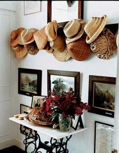 hats are hanging on the wall above a table with flowers in vases and pictures