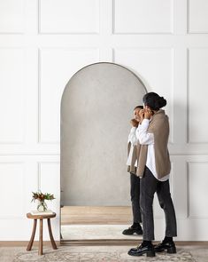 a man standing in front of a mirror while talking on a cell phone and holding his hand up to his face