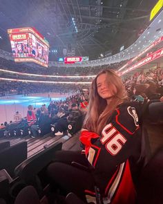 a woman sitting in the stands at an ice hockey game wearing a jersey with numbers on it