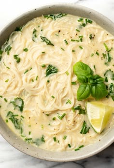 a bowl filled with pasta and spinach on top of a marble countertop next to a lemon wedge