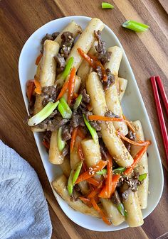 a white plate topped with pasta covered in meat and veggies next to chopsticks