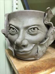 a clay pot with a face on top of a wooden table next to a wall