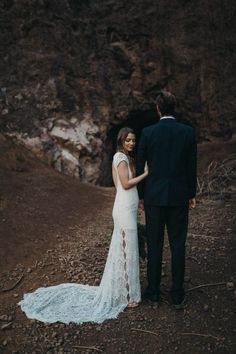 a bride and groom standing in front of a cave