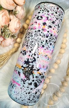 the pink and black speckled tumbler is next to some flowers on a white fur