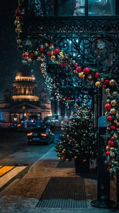 christmas trees are decorated with ornaments and lights on the side of a building at night