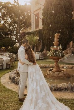 a bride and groom standing in front of a fountain at their wedding reception with the sun shining on them