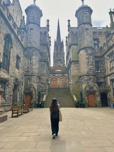 a woman walking in front of an old castle like building with stairs leading up to it