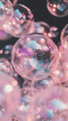 soap bubbles floating in the air on a black surface with pink and blue hues