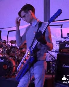 a man standing on stage with a guitar in his hand and other musical instruments behind him