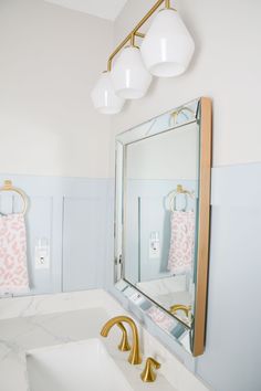 a white bathroom with gold fixtures and marble counter tops, along with pink towels hanging on the wall