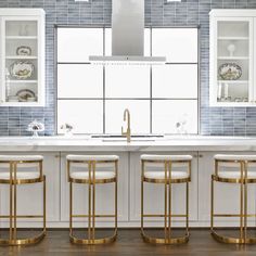 a kitchen with white counter tops and gold barstools in front of a window