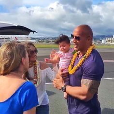 a man holding a baby in his arms while standing next to other people on an airport tarmac