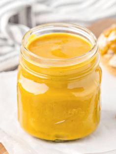 a jar filled with yellow liquid sitting on top of a wooden table next to bread