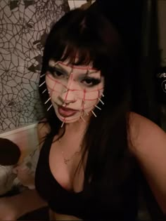 a woman with black hair and makeup has her face taped to the wall by nails