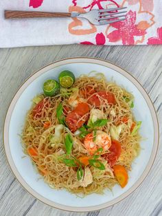 a white plate topped with noodles and vegetables next to a fork on top of a wooden table