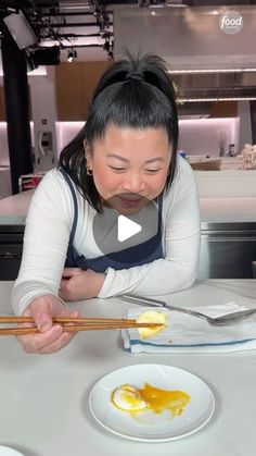 a woman sitting at a table with chopsticks in front of her and an egg on the plate