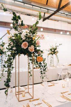 an arrangement of flowers and greenery in gold vases on a white table cloth