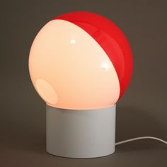 a red and white lamp sitting on top of a table next to a gray wall