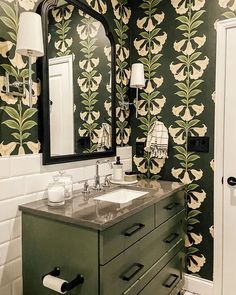 a bathroom with green and white wallpaper has a sink, mirror, and cabinet