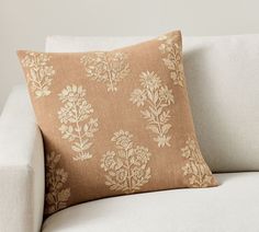 a white couch with a tan floral pillow on it