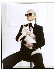 a woman in a suit and sunglasses holding a white cat while sitting on a chair