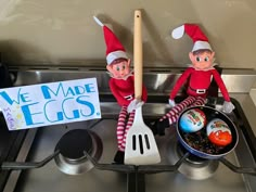 two elfs sitting on top of a stove with eggs in a pan and a sign that says we made eggs