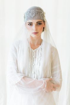 a woman in a white dress and veil with her arms crossed, looking at the camera