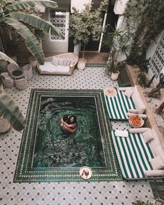 a man is in the middle of a pool surrounded by lounge chairs and potted plants