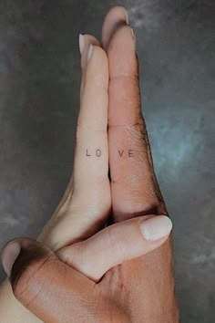 two hands holding each other with the word love tattooed on their thumbnails in front of them